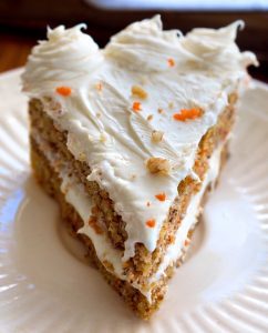 Moist carrot cake slice with cinnamon tones, often topped with cream or frosting.